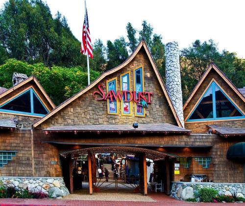 A rustic building with a sign reading "Sawdust," featuring a stone chimney and colorful windows, surrounded by greenery.