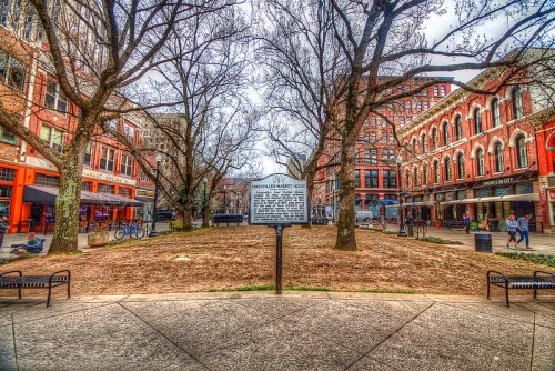 A historic market square with a sign, surrounded by bare trees and brick buildings, in an urban setting.