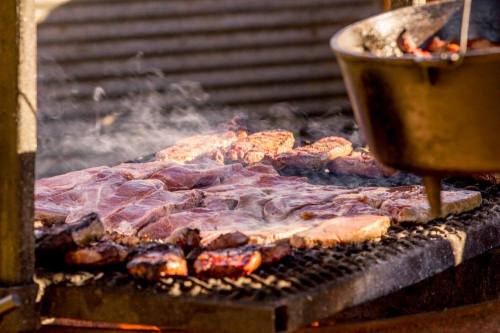 Grilling meat on a barbecue with smoke rising, alongside a pot cooking over an open flame.