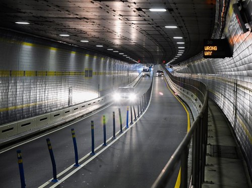 A dimly lit tunnel with vehicles, featuring a sign indicating "WRONG WAY" and reflective tiled walls.