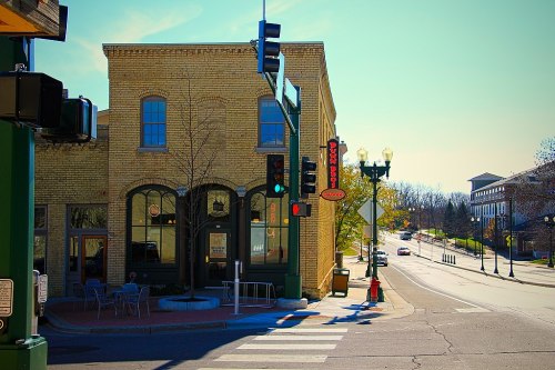 A street corner featuring a brick building, traffic lights, and outdoor seating on a sunny day.