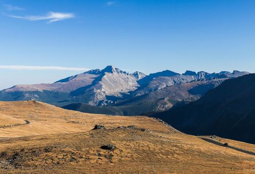 A panoramic view of rugged mountains under a clear blue sky, with golden grasslands in the foreground.
