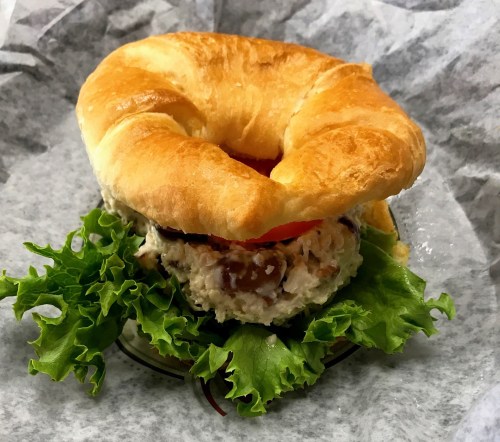 A croissant sandwich filled with chicken salad, lettuce, and tomato, served on a bed of leafy greens.