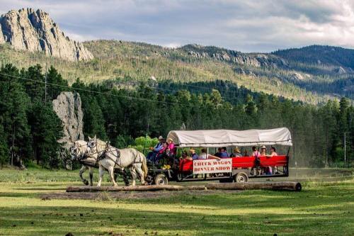 A horse-drawn wagon carries guests through a scenic landscape, featuring mountains and trees, for a dinner show experience.