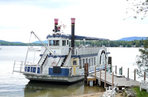 A paddleboat docked at a lakeside pier, surrounded by calm water and distant hills under a cloudy sky.