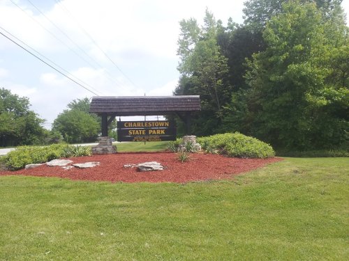 Sign for Charlestown State Park surrounded by green grass and landscaped flower beds. Trees in the background.
