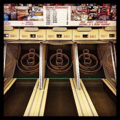 Three skee ball lanes with scoreboards above, featuring wooden ramps and circular targets for scoring.