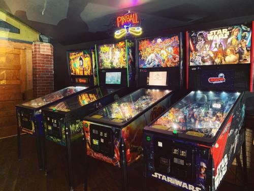 A row of colorful pinball machines featuring various themes, illuminated by a neon "Pinball" sign above.