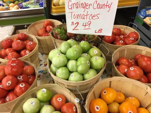 Baskets of colorful tomatoes, including red, green, and orange, with a sign displaying the price of $2.49 per pound.