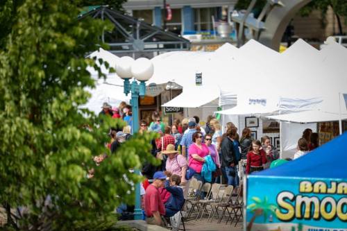 A bustling outdoor market with white tents, vendors, and a crowd of people enjoying the event.