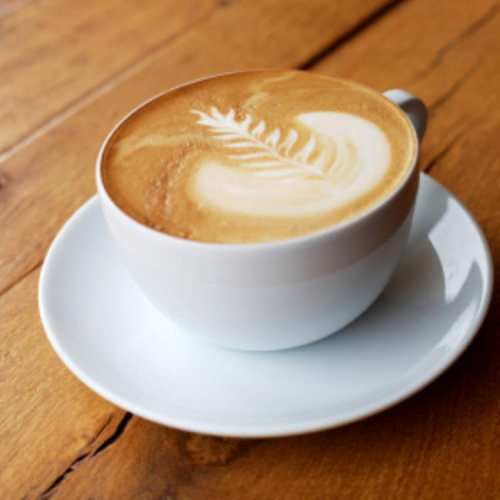 A white cup of latte art featuring a leaf design, placed on a white saucer on a wooden table.