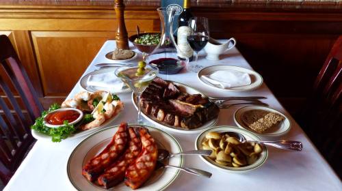 A beautifully set table with a variety of dishes, including grilled meats, shrimp, olives, and wine.