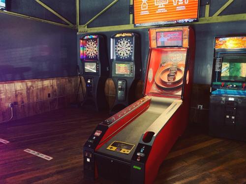 A dimly lit arcade featuring a skee-ball machine, dart boards, and vintage arcade games against a wooden backdrop.