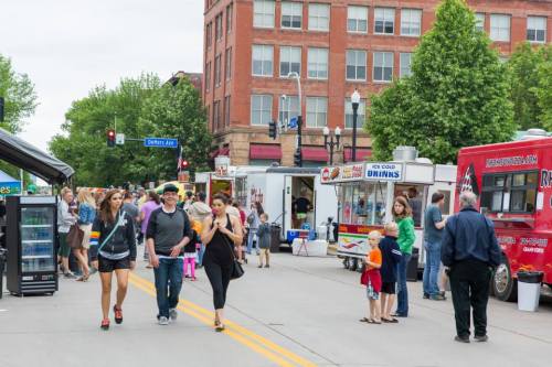 A bustling street scene with food trucks, vendors, and people walking, enjoying a community event on a cloudy day.
