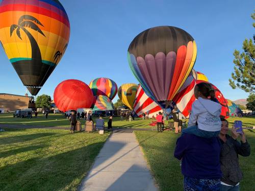 A colorful array of hot air balloons fills the sky, with people enjoying the event on a sunny day.