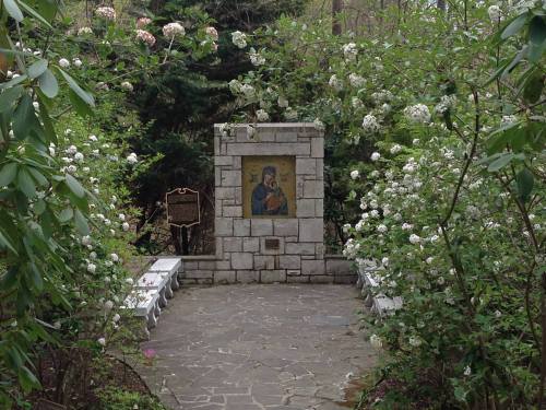 A stone structure with an icon surrounded by blooming flowers and benches in a serene garden setting.