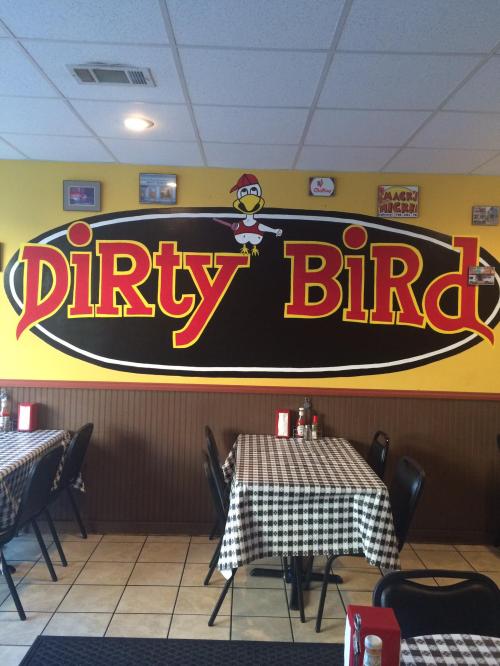 Interior of a restaurant featuring a large "Dirty Bird" sign on the wall, with checkered tablecloths and empty tables.