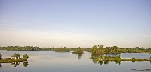 A serene lake surrounded by lush greenery and small islands under a clear blue sky.