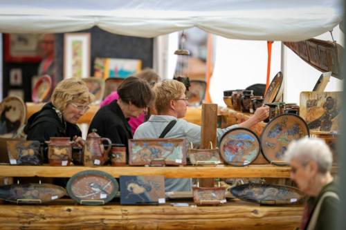 A group of women browsing handmade pottery and art at a market stall.