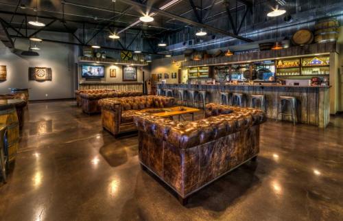 A stylish bar interior featuring leather couches, a wooden bar, and dartboard, with modern industrial decor.