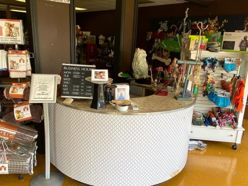 A pet store checkout area with a curved counter, business hours sign, and various pet supplies displayed.
