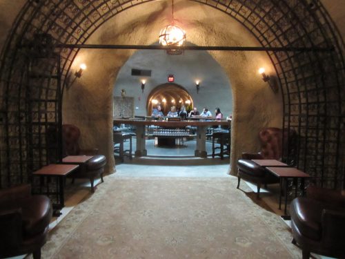 A dimly lit, arched wine cellar with leather chairs and a view of a bar area in the background.