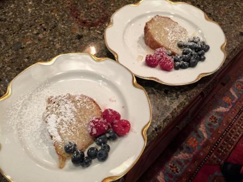 Two plates of French toast topped with powdered sugar and fresh raspberries and blueberries on a granite countertop.