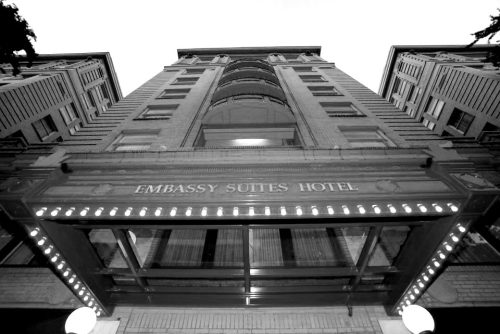 Black and white image of the Embassy Suites Hotel entrance, showcasing its architectural details and marquee lights.