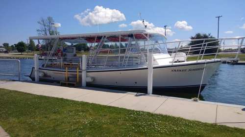 A white boat named "Yankee Sunshine" docked at a marina on a sunny day, with green grass and blue sky in the background.