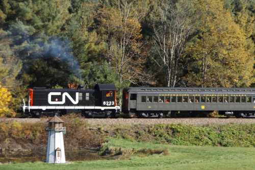 A black and red CN locomotive pulls a vintage passenger car along a scenic route with trees in the background.