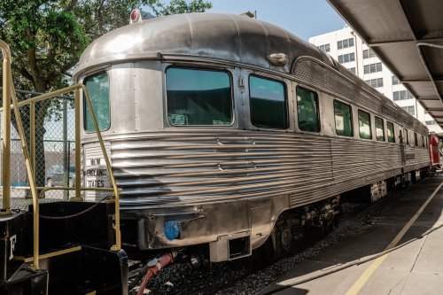 A vintage silver train car parked at a station, showcasing its streamlined design and large windows.