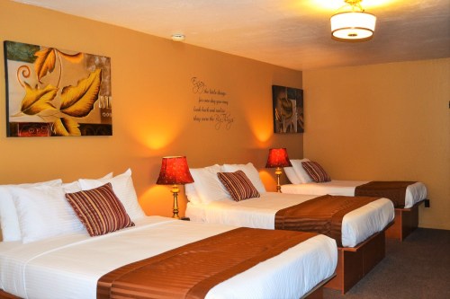 A cozy hotel room with three beds, warm lighting, and decorative artwork on the walls.