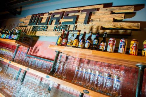 A wooden bar with a sign reading "WORST" and shelves lined with various beer bottles and glasses.