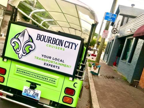 A green vehicle with a sign reading "Bourbon City Cruisers" parked on a street, promoting local transport services.