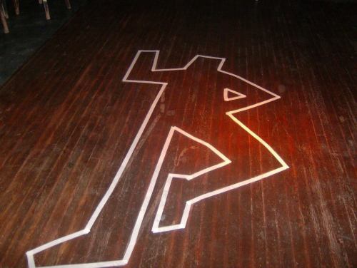A wooden floor with a white outline of a running figure, illuminated by a warm light.
