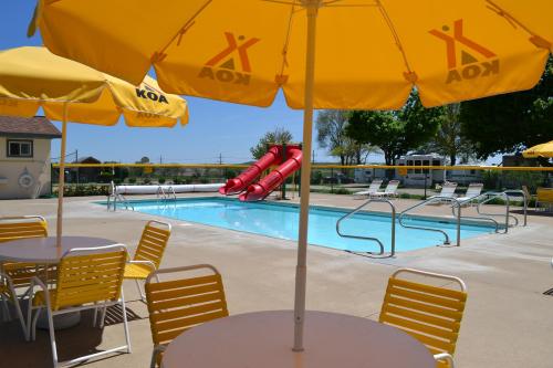 A sunny pool area with yellow umbrellas, lounge chairs, and red water slides beside a clear blue pool.