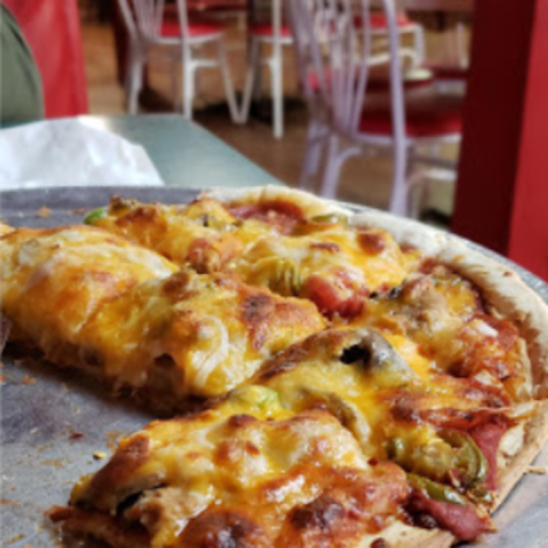 A close-up of a cheesy pizza topped with vegetables, served on a metal tray in a casual dining setting.