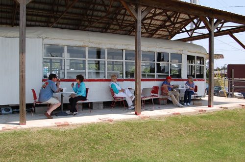 A group of people sitting on chairs outside a vintage train car, enjoying conversation on a sunny day.
