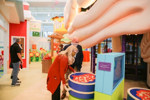 Two adults interact with colorful, oversized play equipment in a vibrant, child-friendly indoor space.