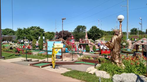 A vibrant mini-golf course featuring various themed holes and a golden statue resembling the Statue of Liberty.