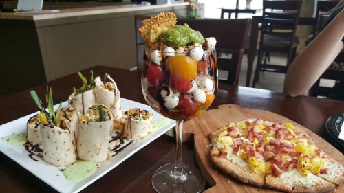 A colorful dessert in a glass with fruit and cream, alongside a plate of wraps and a flatbread pizza with toppings.