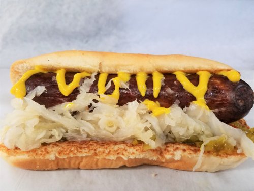 A hot dog in a bun topped with mustard, sauerkraut, and relish on a white background.