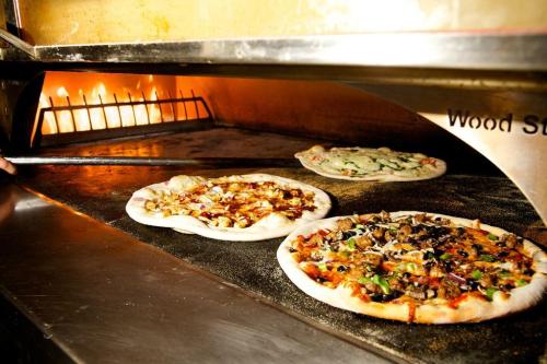 Three pizzas baking in a wood-fired oven, with flames visible in the background.