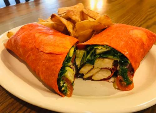 A vibrant red wrap filled with chicken, lettuce, and tomatoes, served with crispy potato chips on the side.