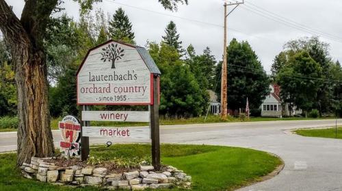 Sign for Lautenbach's Orchard Country, featuring a winery and market, surrounded by trees and a rural road.
