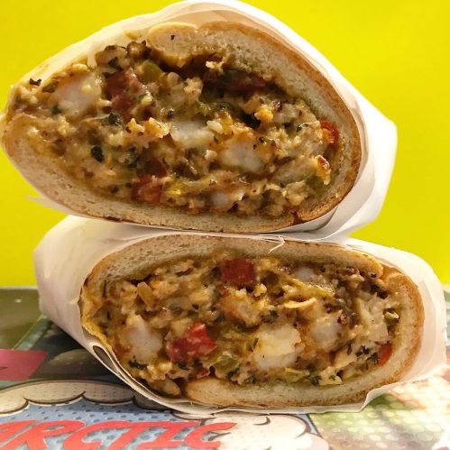 A cross-section of a sandwich filled with shrimp, vegetables, and spices, wrapped in soft bread against a bright background.