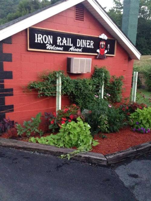 A red diner building with a sign reading "Iron Rail Diner" and colorful flowers in front.