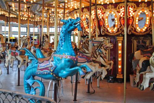 A colorful carousel featuring a blue horse and other ornate animals, illuminated by bright lights.