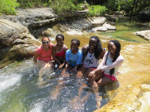 A group of five people enjoying a sunny day by a natural pool surrounded by rocks and greenery.