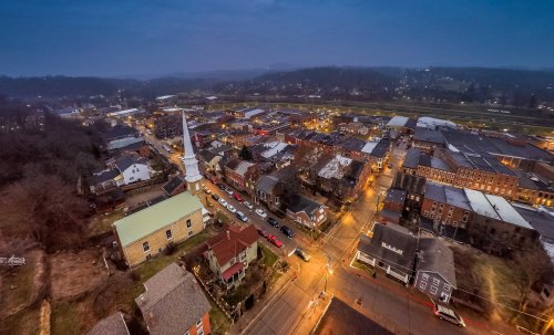 Aerial view of a small town at dusk, featuring streets lined with buildings and illuminated by streetlights.